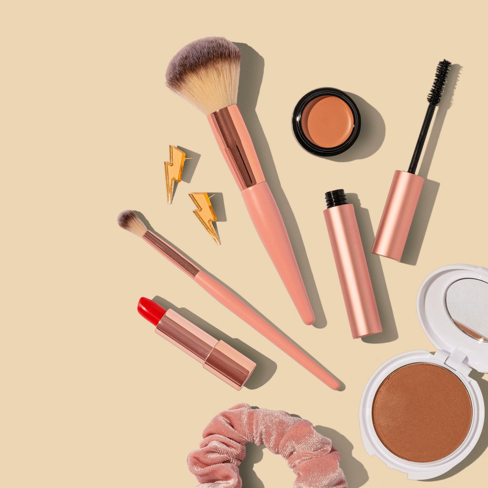 Rose-gold brushes, lipstick and powder on a nude background
